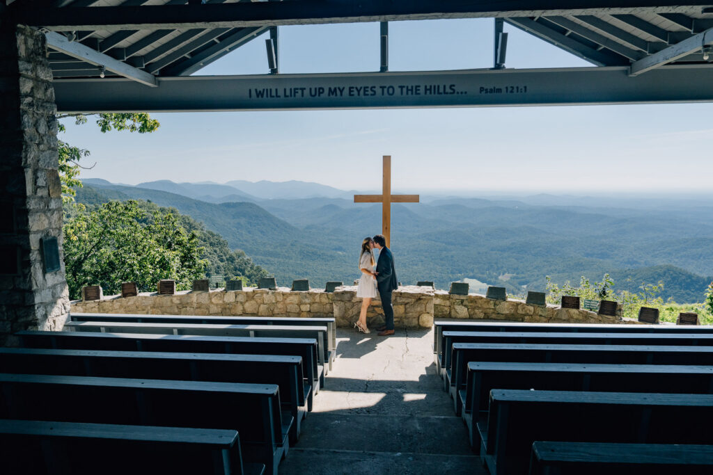 couple kisses in front of a large cross at pretty place chapel in sc
